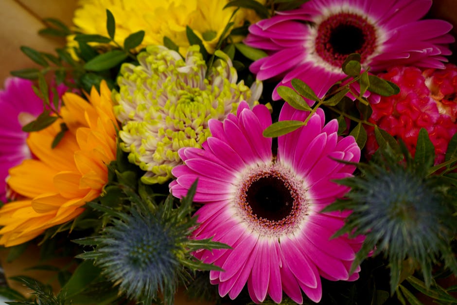 A vibrant floral arrangement featuring large pink gerbera daisies with dark centers, complemented by yellow sunflower-like flowers with wide petals, green chrysanthemums with clustered light green pet